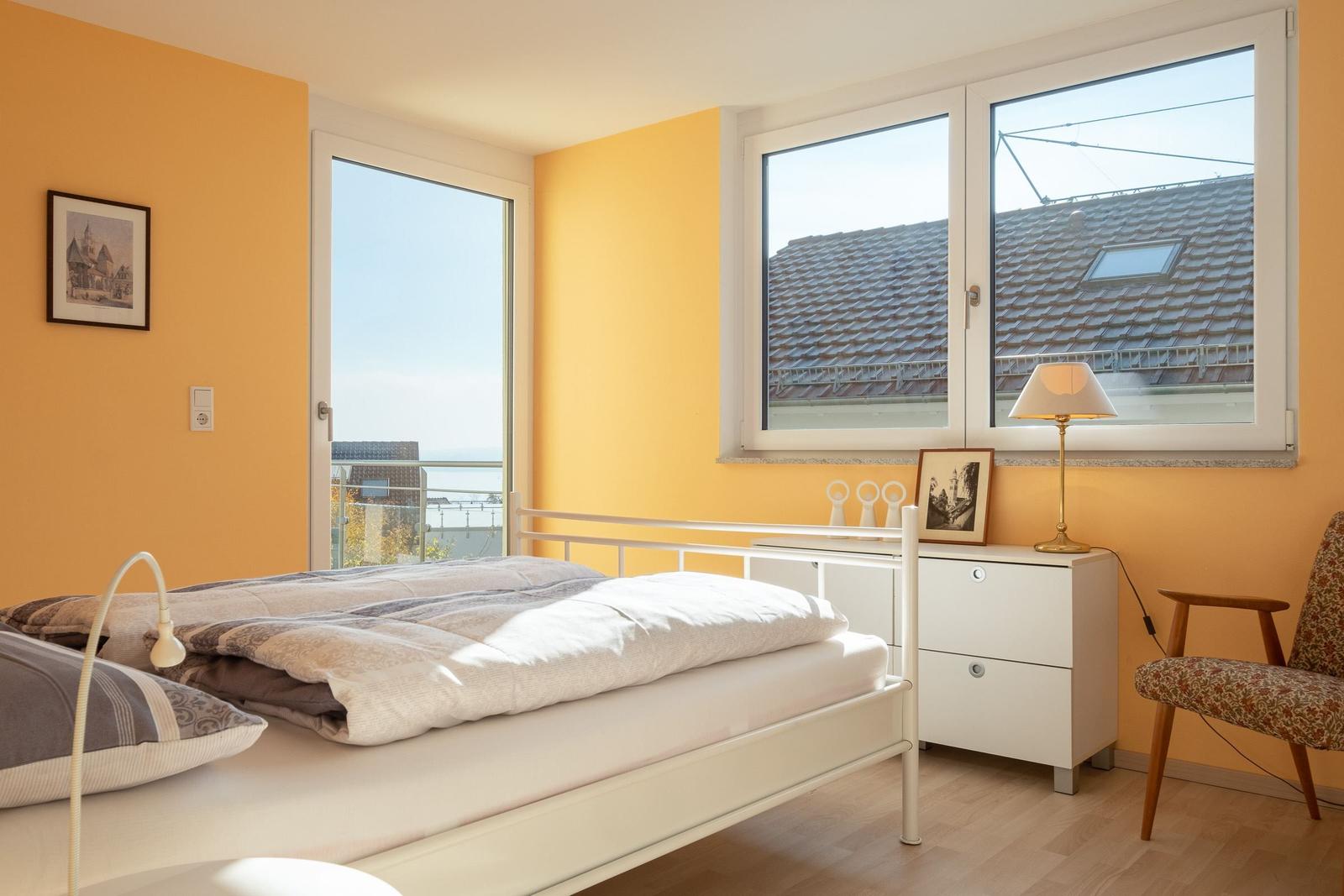 Schlafzimmer mit Bett, Schreibtisch und Fensterblick auf Dach