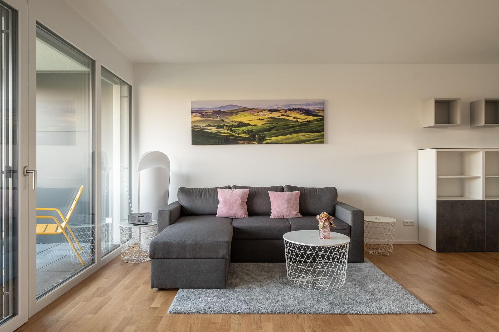 Wohnzimmer mit grauem Sofa, rosa Kissen und großem Landschaftsbild an der Wand.