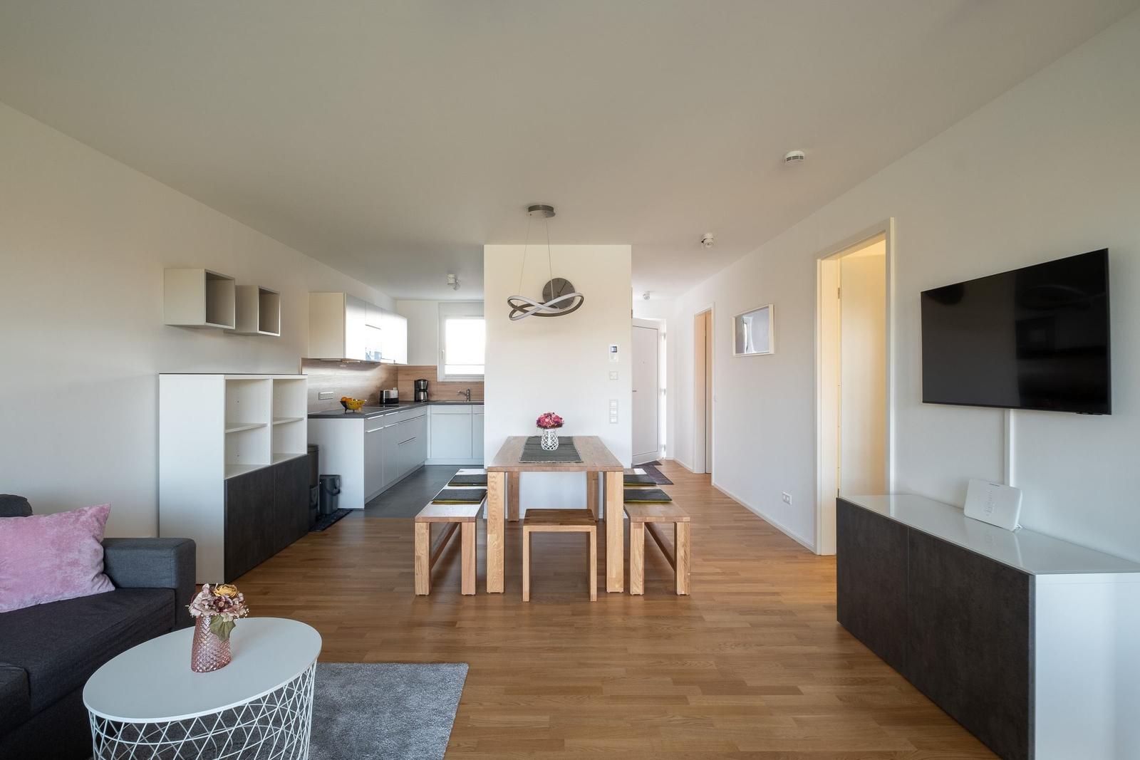 Wohnküche mit Esstisch, Sofa und TV. Holzfußboden und helle Wände.