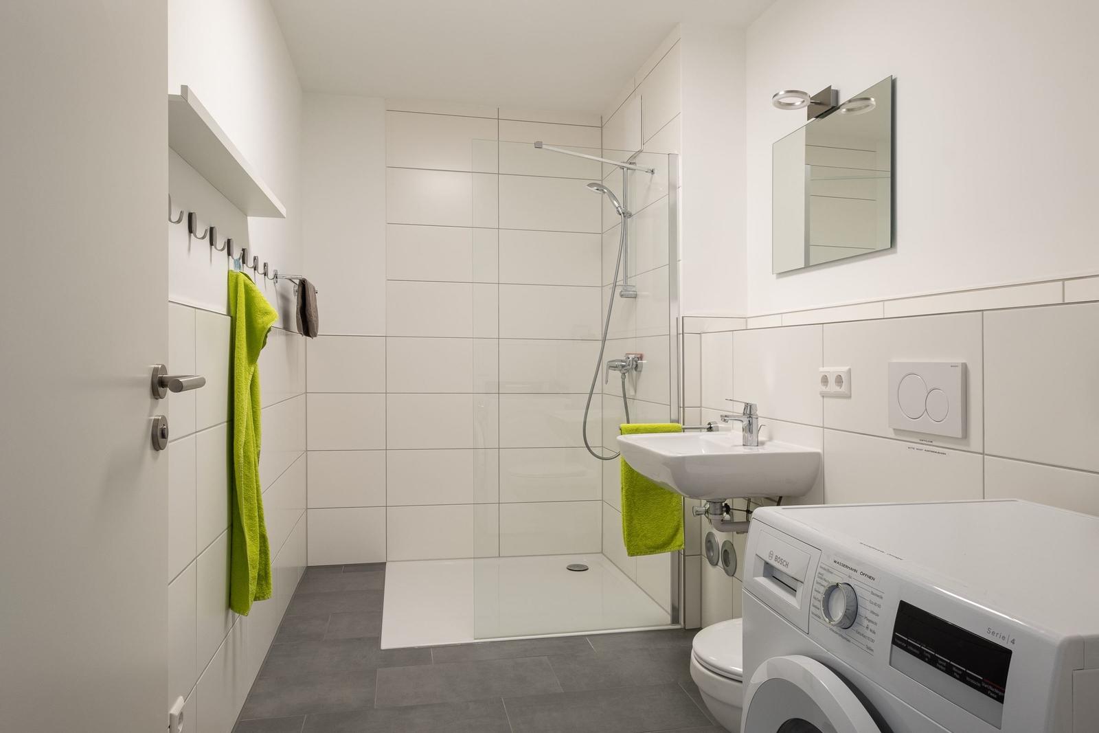 Badezimmer mit Dusche, Waschbecken und Waschmaschine.