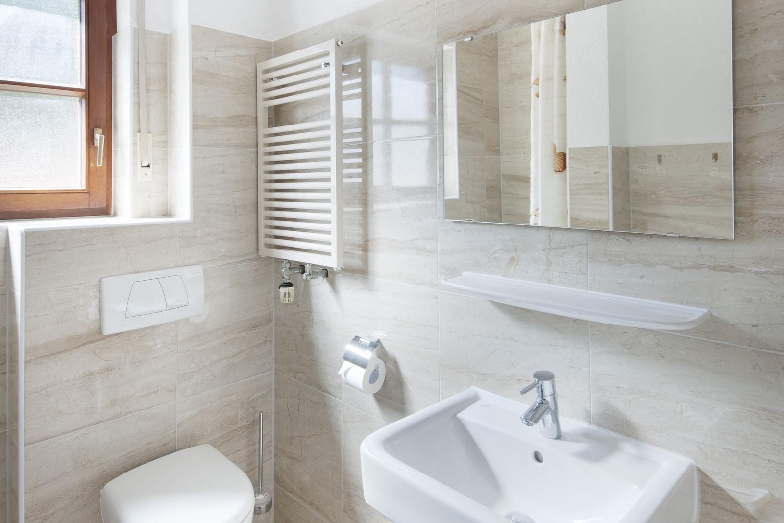 Badezimmer mit Toilette, Waschbecken und Spiegel an hellen Wandfliesen.