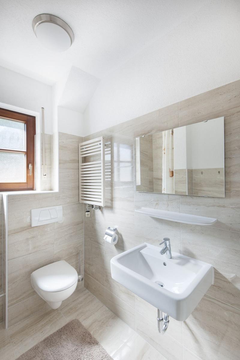 Badezimmer mit Toilette, Waschbecken und Spiegel. Holzfenster und Heizkörper.
