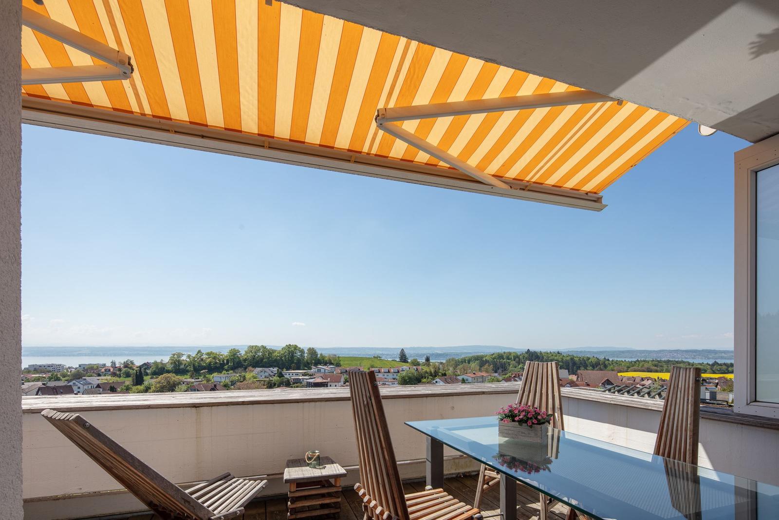 Terrasse mit orangefarbenem Markisenüberdachung, Tisch und Stühle mit Blick auf Landschaft.