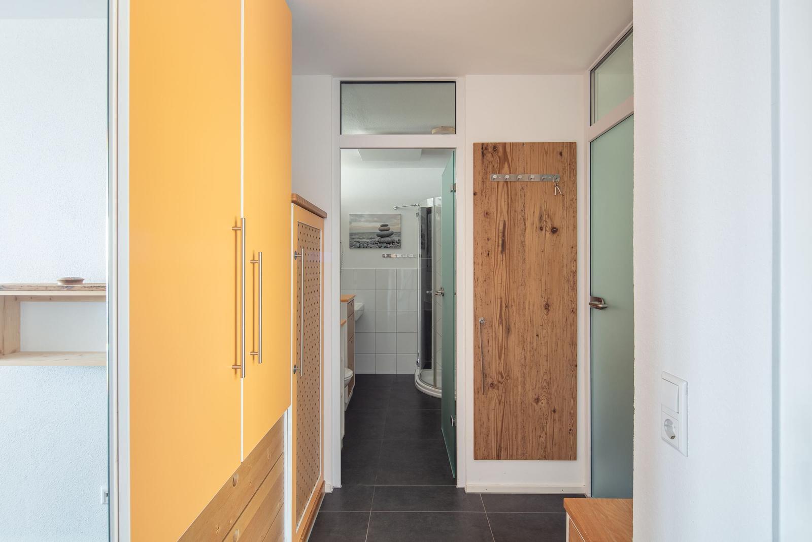 Flur mit Holztür, gelbem Schrank und Blick in die Dusche.
