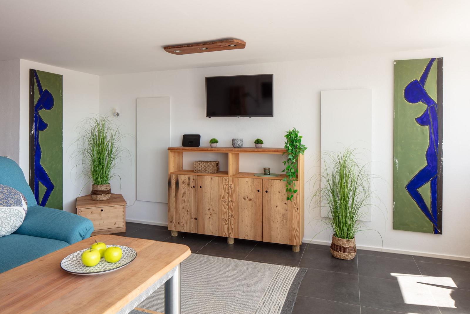 Wohnzimmer mit Holzmöbeln, Fernseher und Pflanzen an den Wänden.
