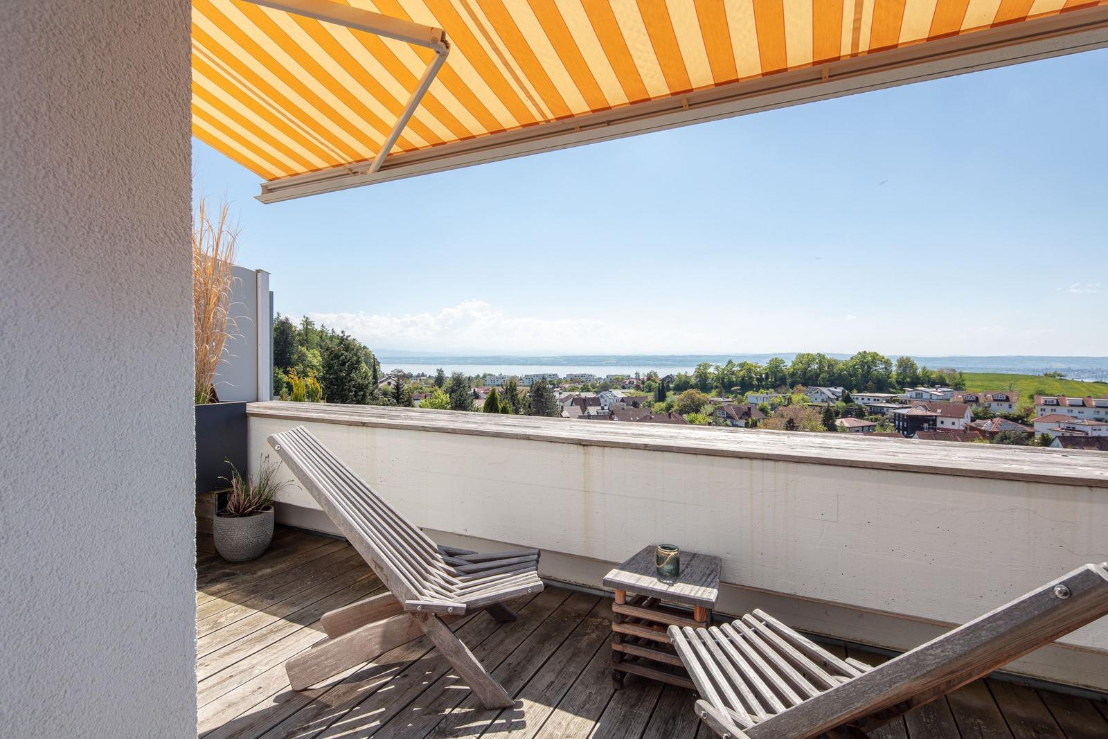 Terrasse mit Sonnenschutz, Liegestühlen und Blick auf See und Landschaft.