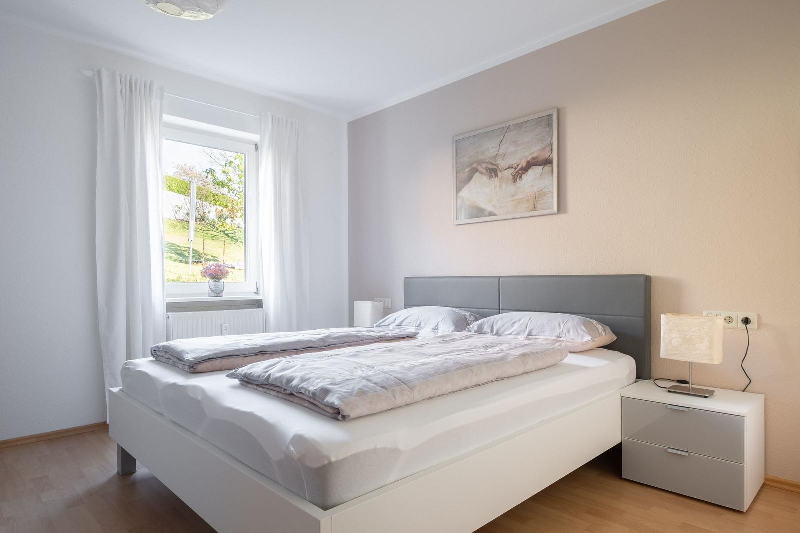 Schlafzimmer mit Doppelbett, Nachttisch und Fenster mit Blick auf Grünfläche.