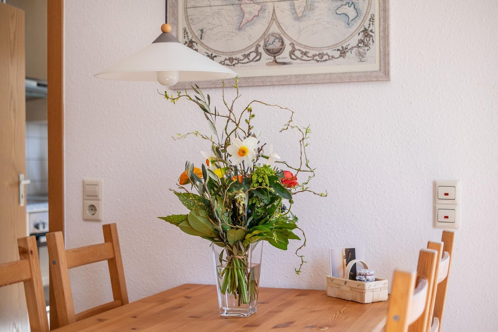 Esstisch mit Blumenarrangement, Holzstühle und Wandbild mit Weltkarte.