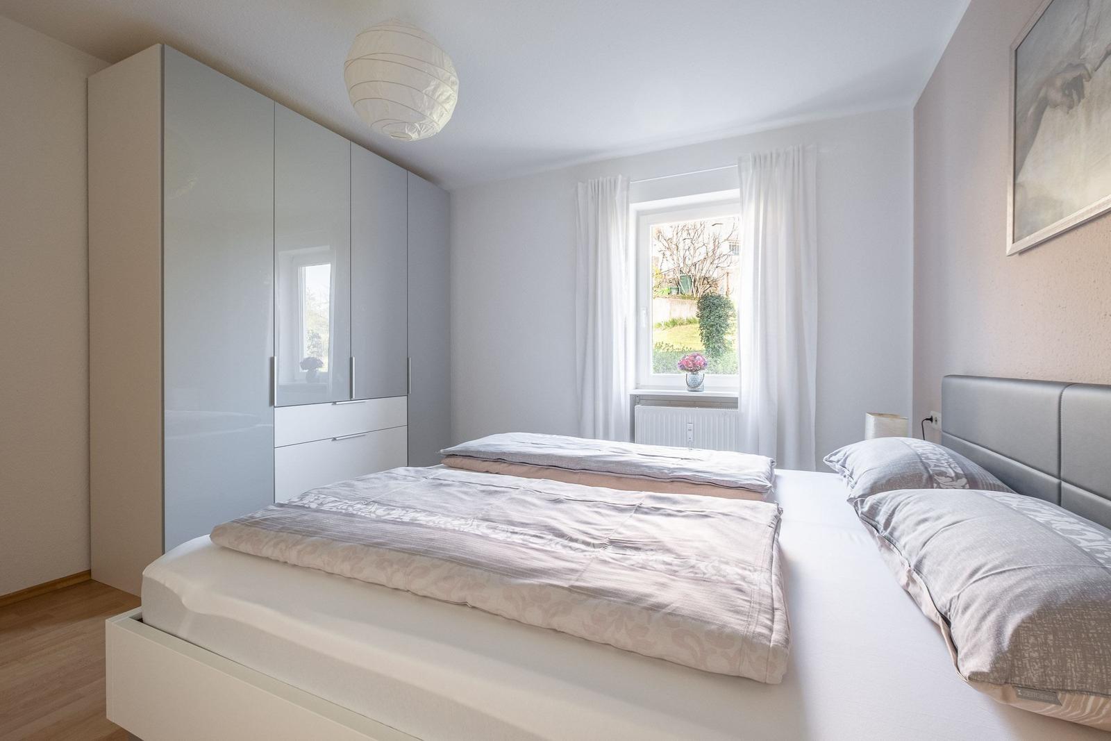 Schlafzimmer mit Doppelbett, Kleiderschrank und Fenster mit Blick auf Garten.