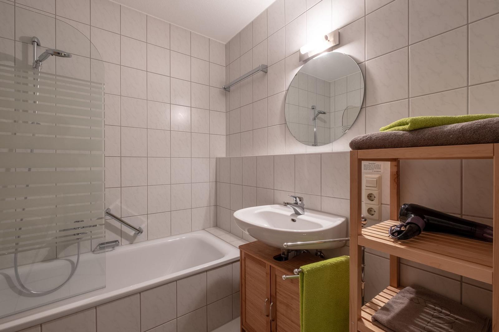 Bad mit Dusche, Waschbecken und Holzregal mit Handtüchern.