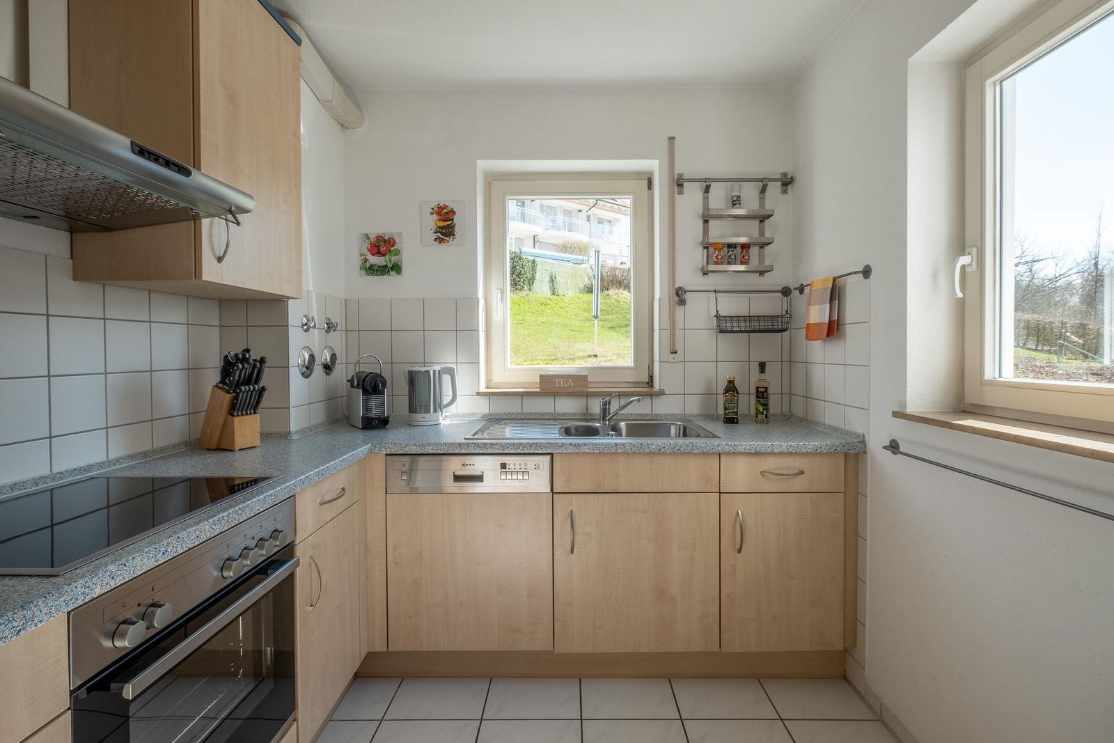 Küche mit Holzschränken, Spüle und Fensterblick auf Grünfläche.
