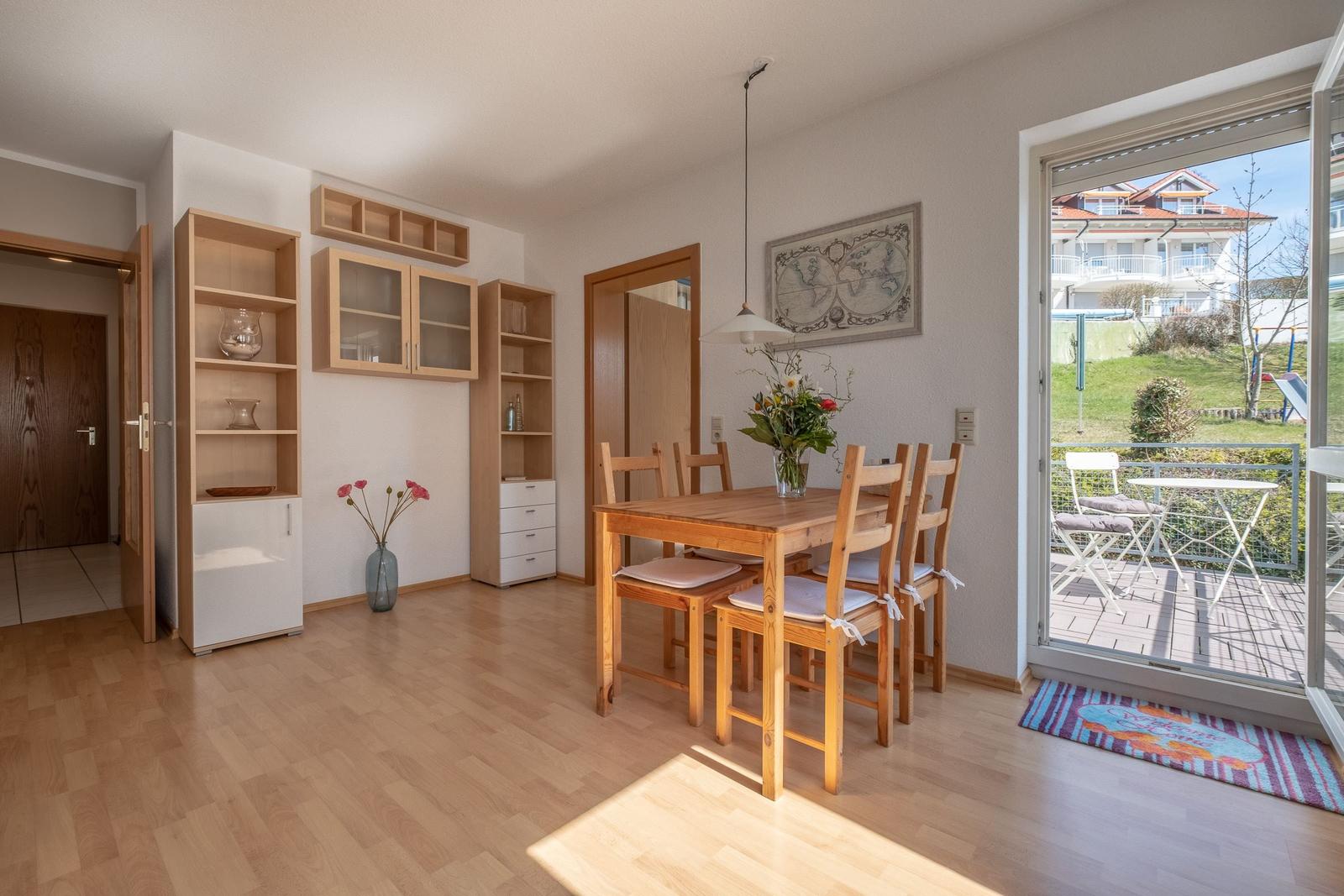 Esszimmer mit Holztisch, Stühlen und Balkonzugang. Hintergrund: Wohnbereich und Küche.