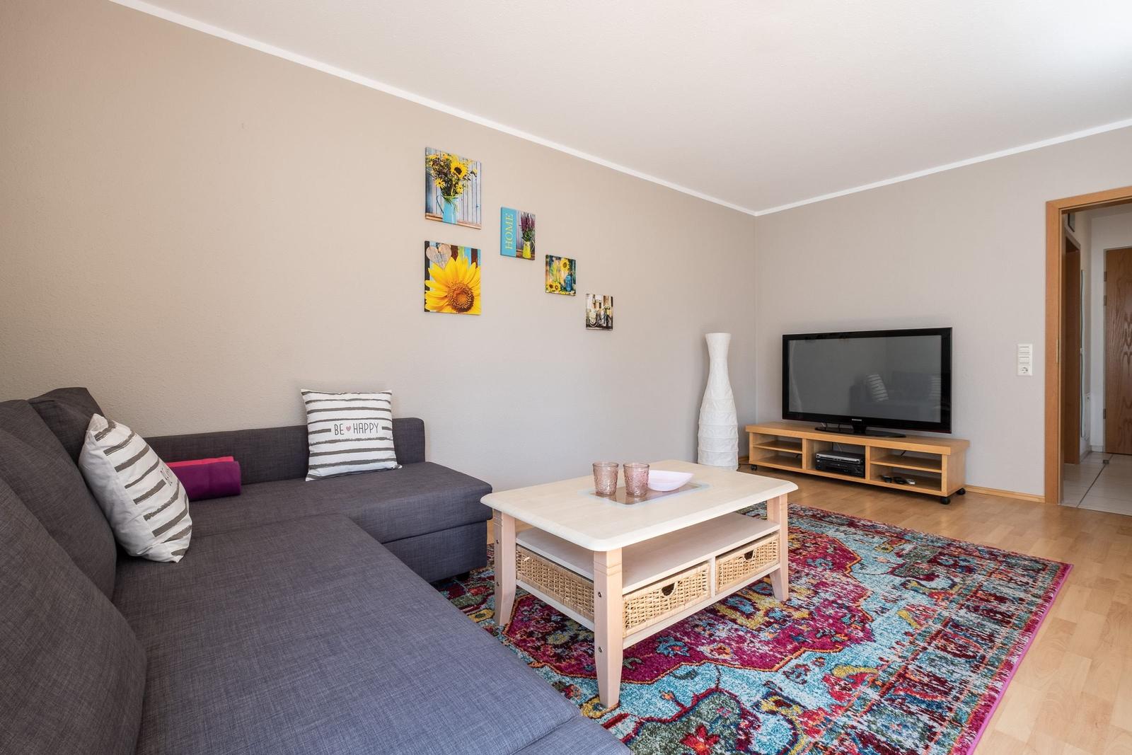 Wohnzimmer mit Sofa, Couchtisch und Fernseher auf Holzregal.