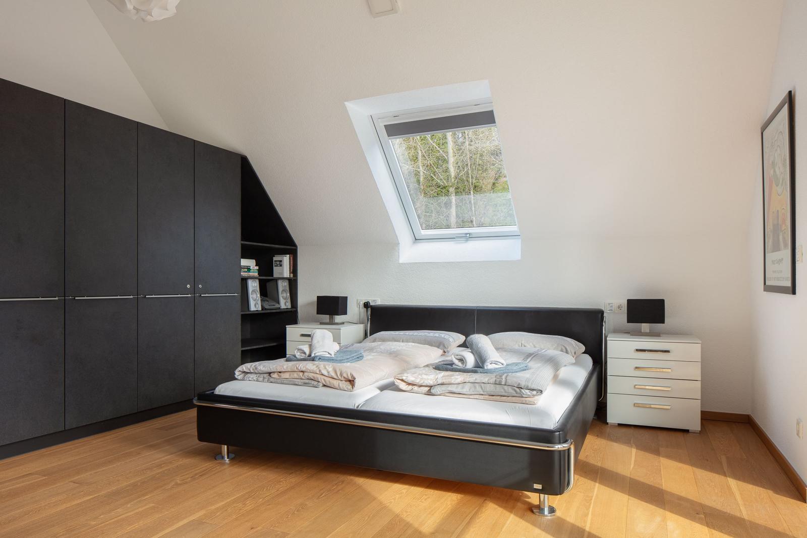 Schlafzimmer mit Dachfenster, Bett, Schrank und Nachttischen.