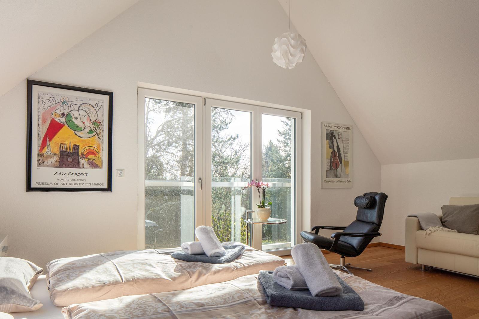 Schlafzimmer mit Balkon, Kunstwerken und Bett mit Handtüchern.