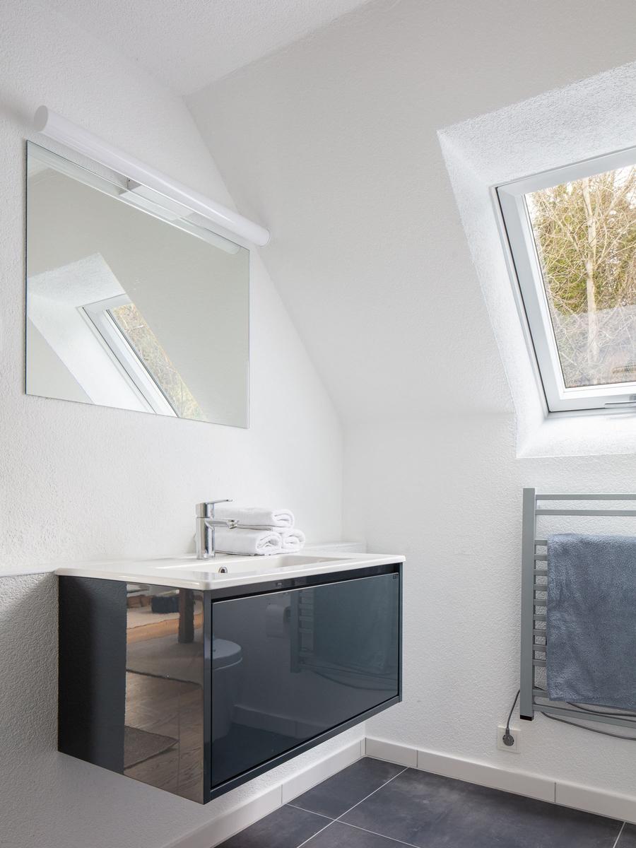 Badezimmer mit Waschbecken, Spiegel und Dachfenster. Handtuchhalter und gefaltete Handtücher.