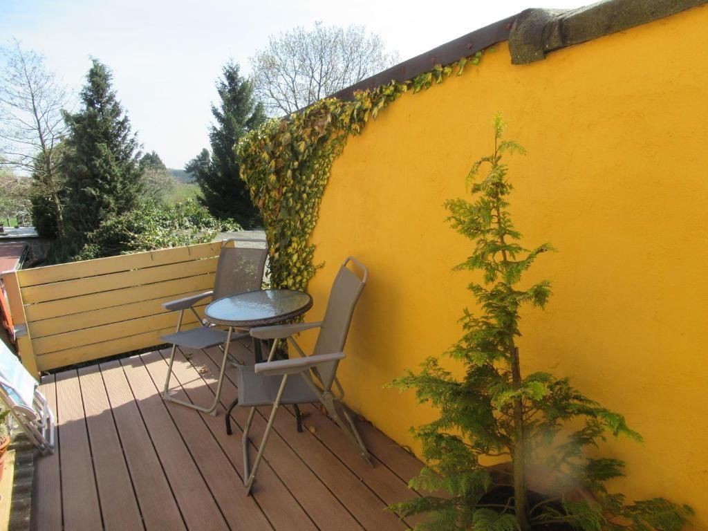 Terrasse mit Tisch und Stühlen, gelber Wand, Pflanzen und Blick auf Bäume.