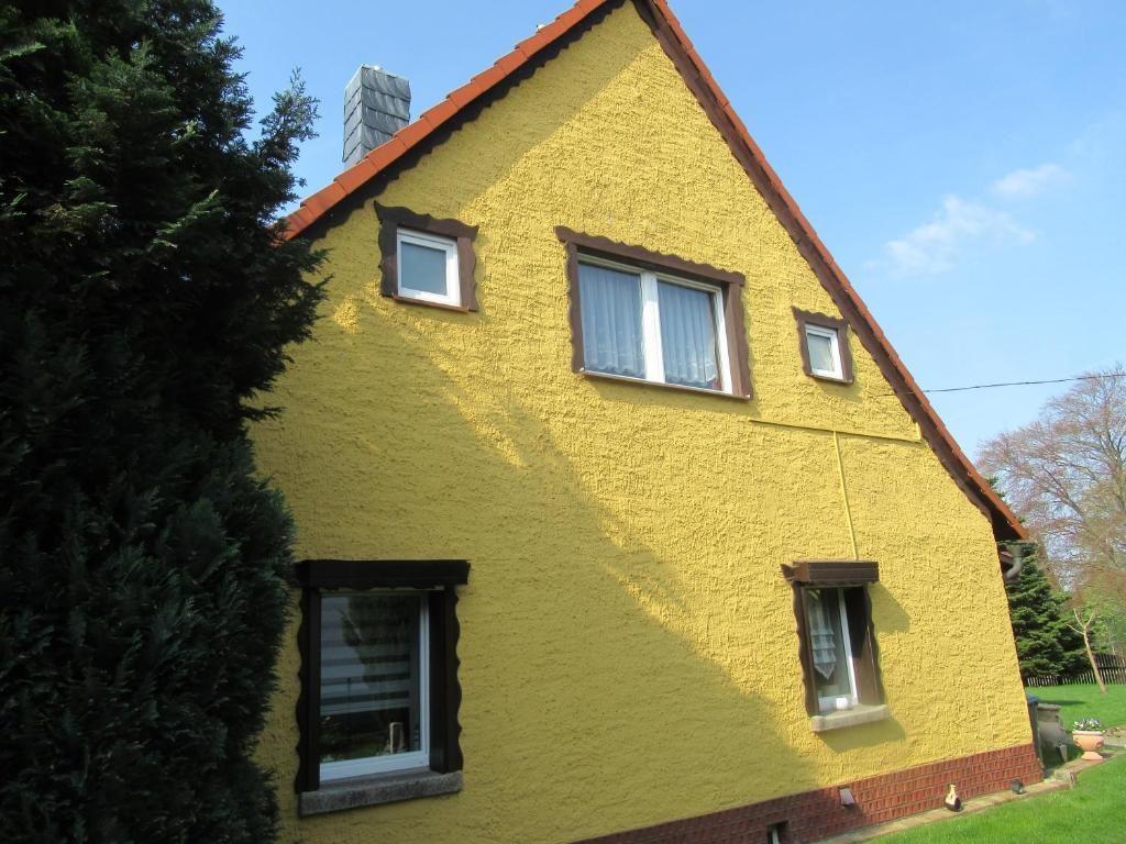 Gelbes Haus mit braunen Fensterrahmen und rotem Dach unter blauem Himmel.