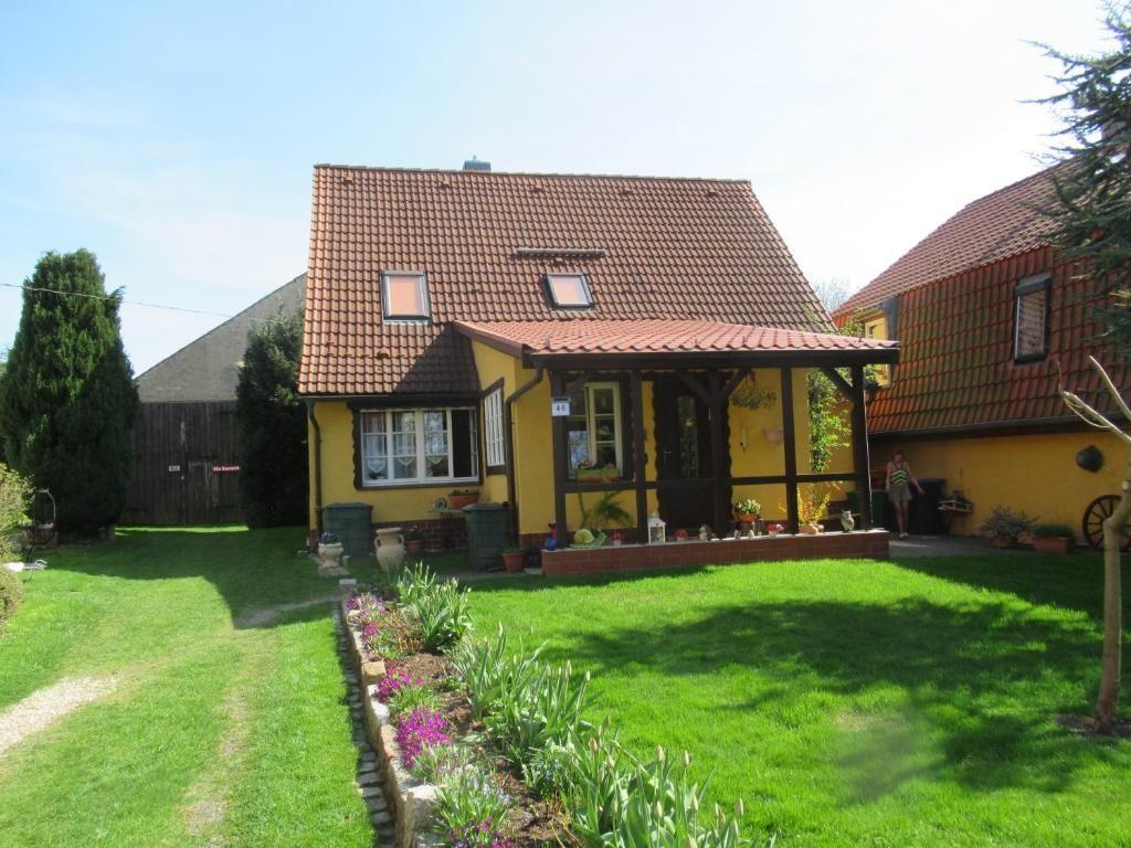 Ein gelbes Haus mit rotem Dach und Garten. Eine Terrasse mit Pflanzen.