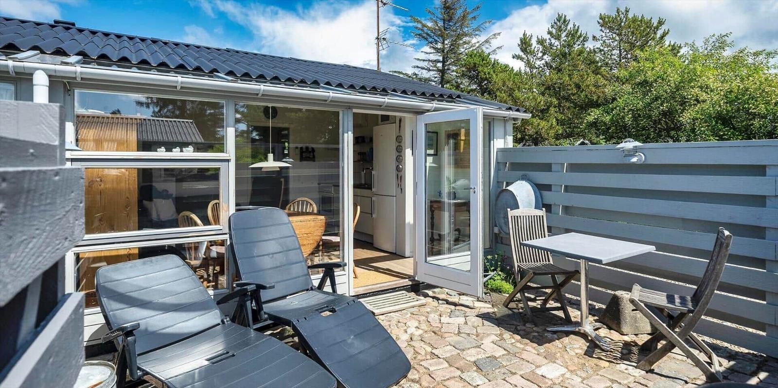 Terrasse mit Liegestühlen und Tisch. Durchgehendes Glasfenster zum Innenraum.