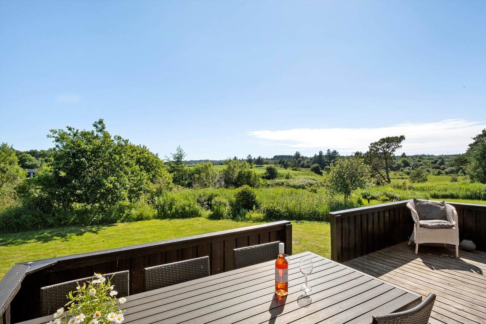 Terrasse mit Tisch, Stühlen und Weinkrug. Blick auf grünes Gelände und Bäume.