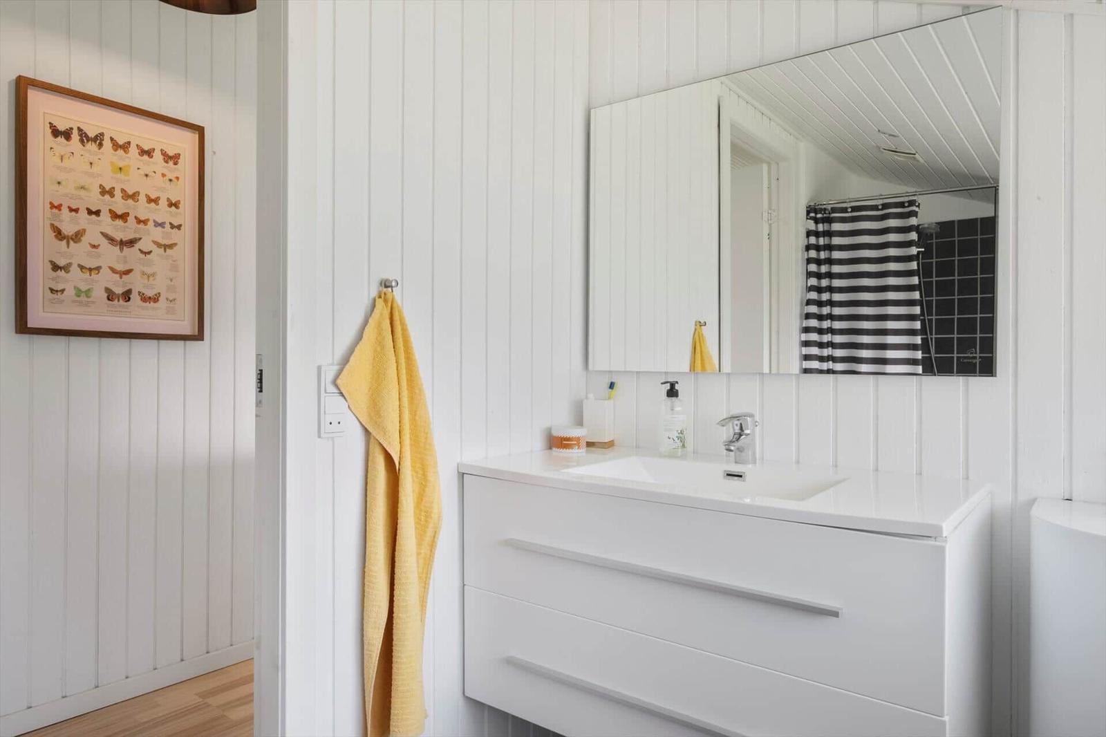 Badezimmer mit weißem Waschbecken, Spiegel und gelbem Handtuch an der Wand.