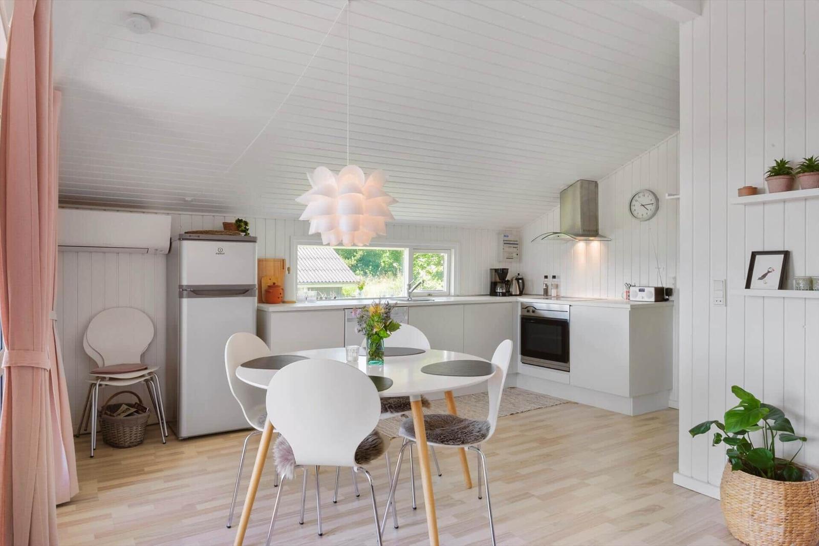 Küche mit Esstisch, Kühlschrank und Fenster. Weiße Wände und Holzboden.