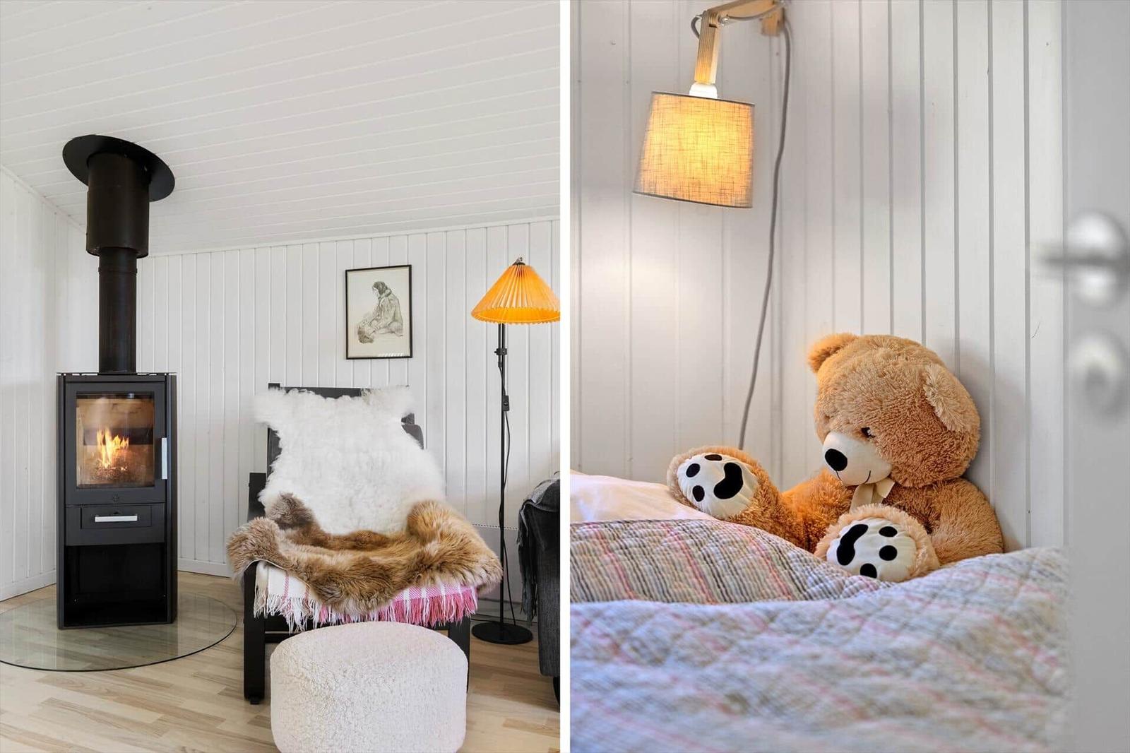 Kamin mit brennendem Holz, Sessel mit Felldecke und Wandlampe. Großer Teddybär auf Bett mit gemustertem Bettzeug.
