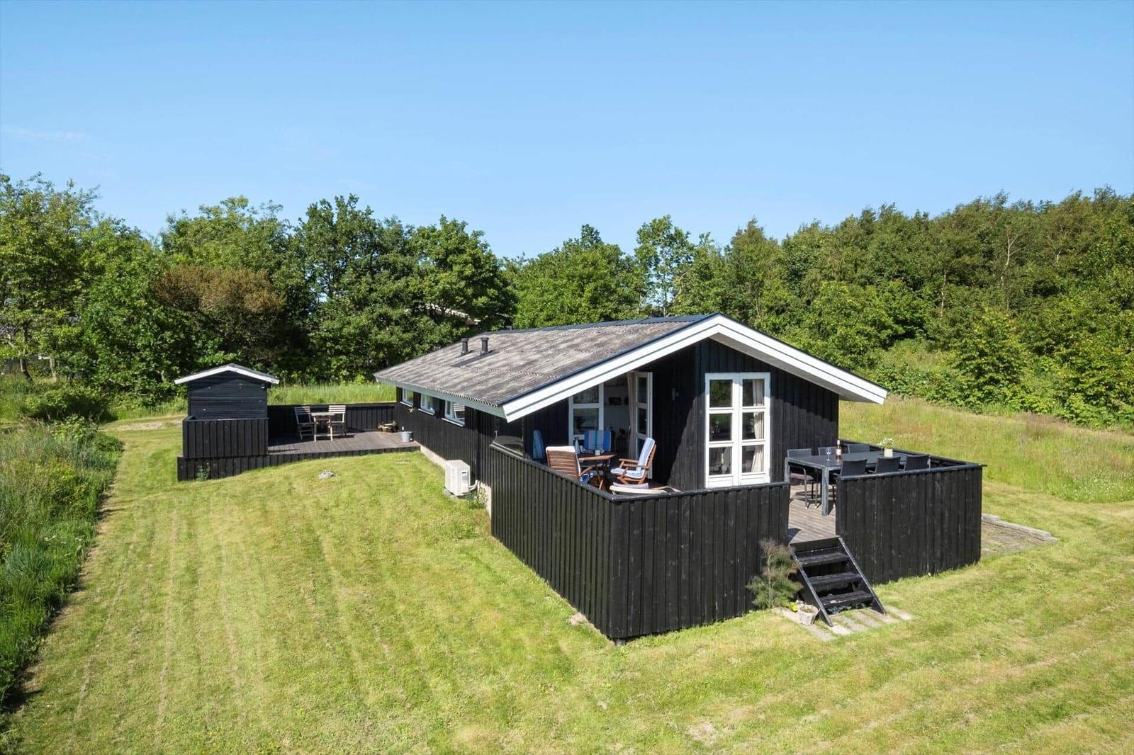 Schwarzes Holzhaus mit Terrasse und Garten. Umgeben von Wald und Gras.