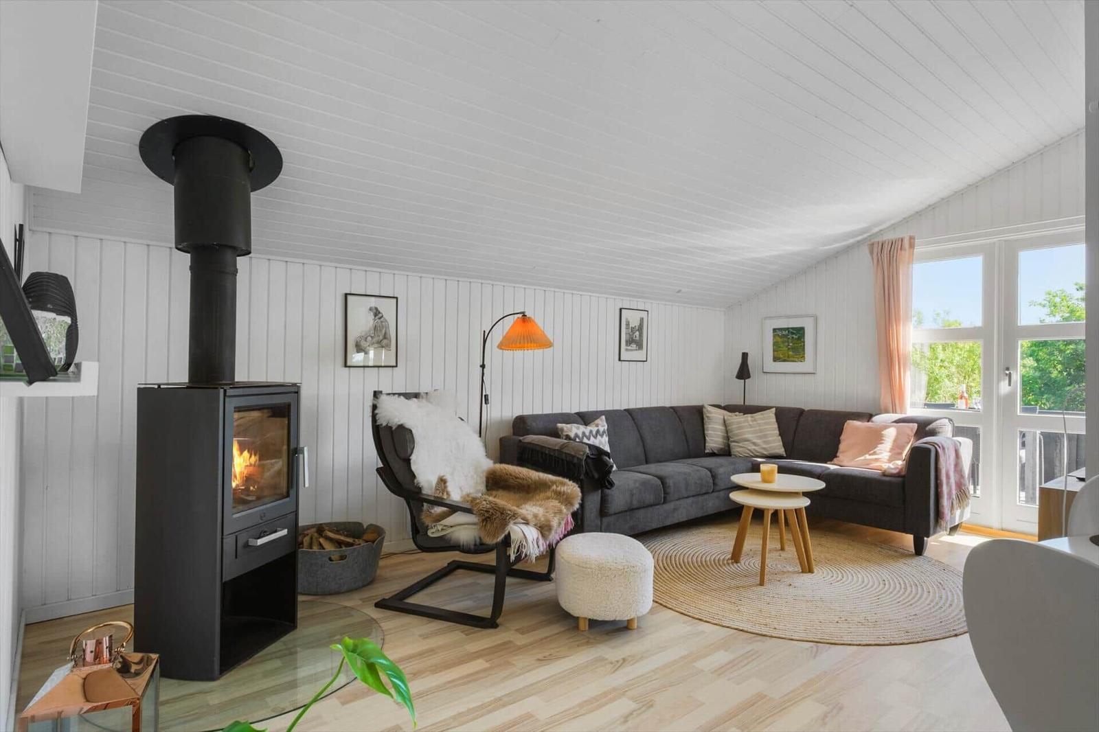 Wohnzimmer mit Kamin, Sofa und Sessel. Holzboden und große Fenster.