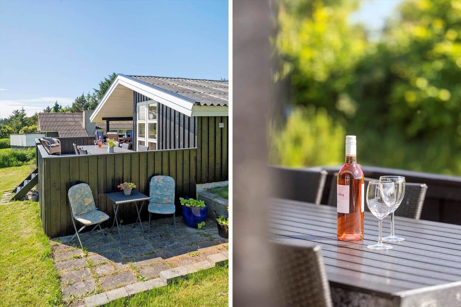 Haus mit Terrasse, Garten und Tisch mit Weinflasche und Gläsern.
