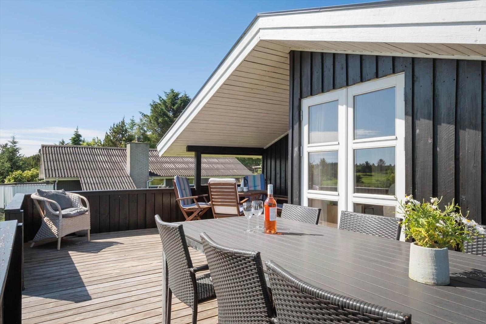 Terrasse mit Tisch, Stühlen und Flasche. Blick auf Haus und Grünflächen.
