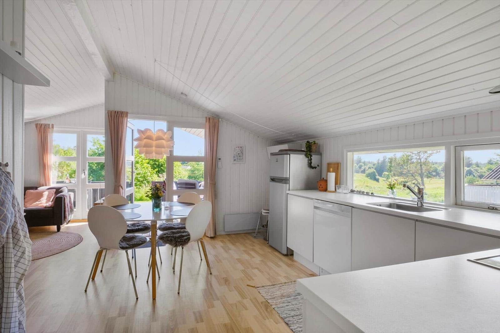Küche mit Essbereich und Blick auf Garten. Holzboden, weiße Einrichtung und Fenster.
