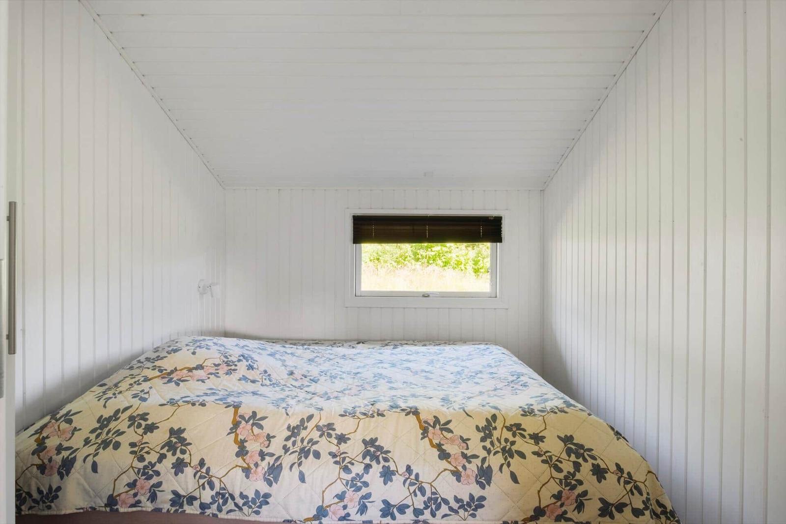Schlafzimmer mit Bett und Fenster. Wände und Decke sind weiß verkleidet.