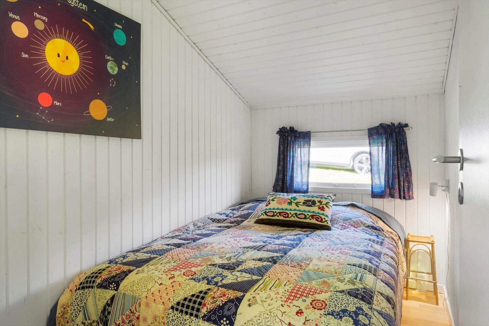 Schlafzimmer mit Bett, Patchwork-Bettwäsche und Sonnensystem-Bild an der Wand.