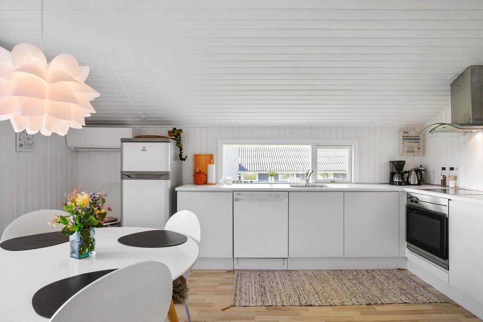 Küche mit Essbereich, weißer Einbauküche, Spüle und Fenster. Holzboden und Decke.