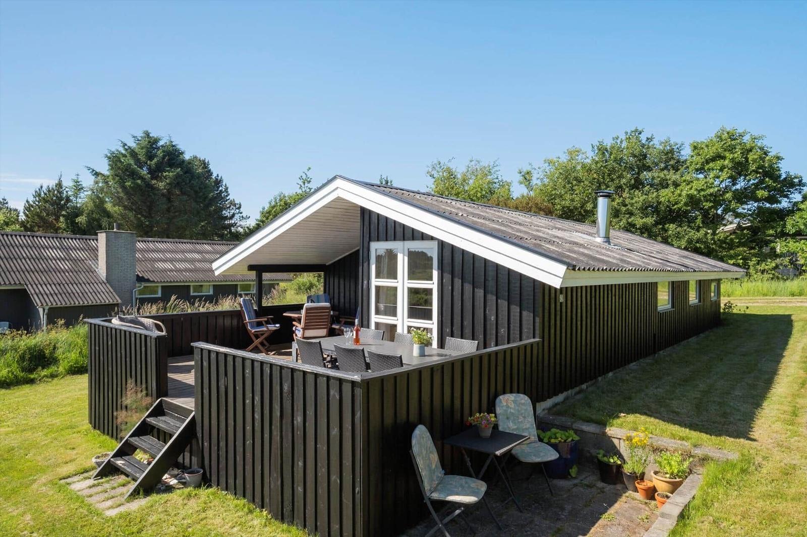 Schwarzer Holzhaus mit Terrasse und Garten. Gartenmöbel und Pflanzen sind sichtbar.