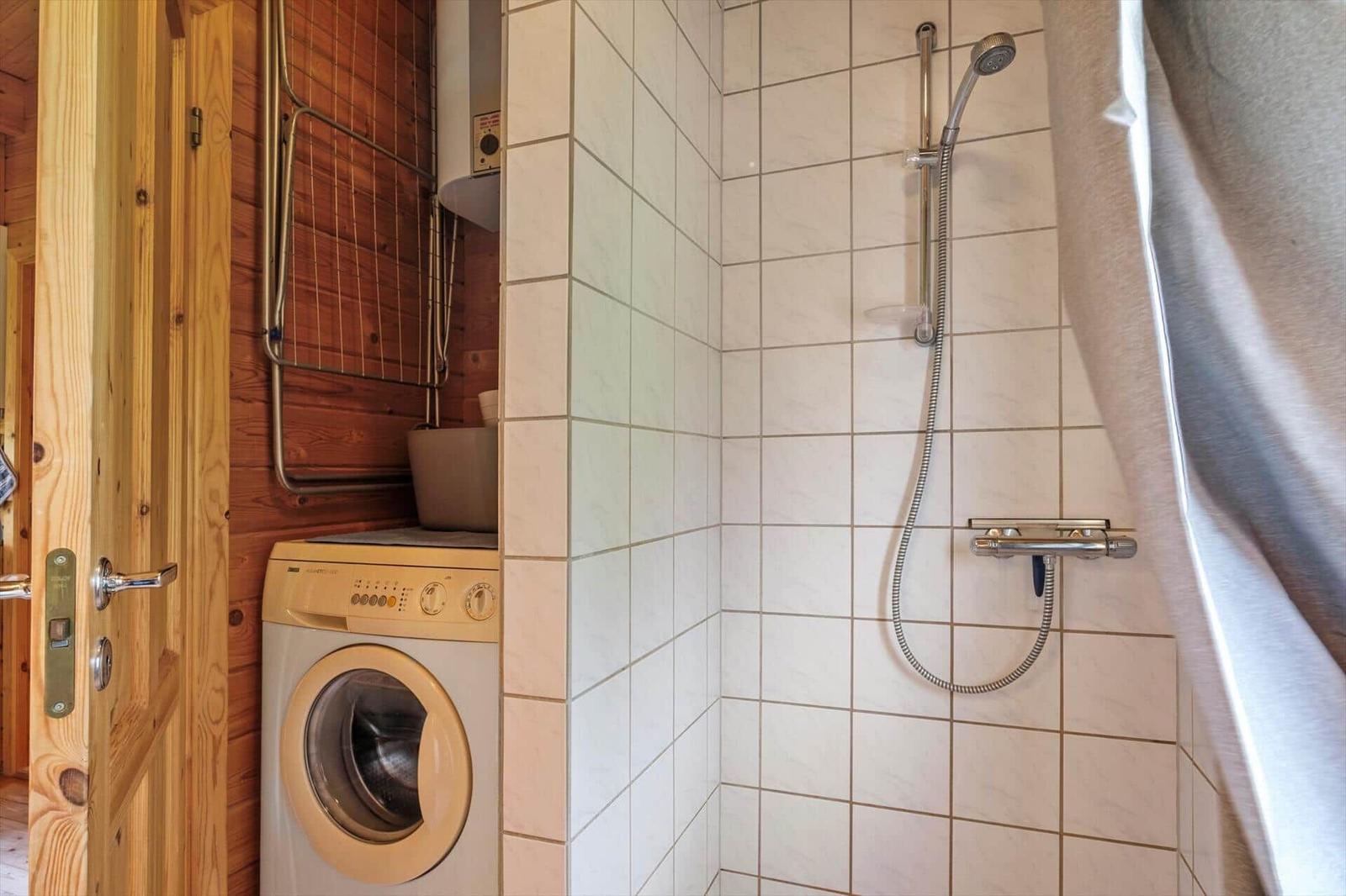 Dusche mit Duschbrause, Waschmaschine und Holzwand im Badezimmer.