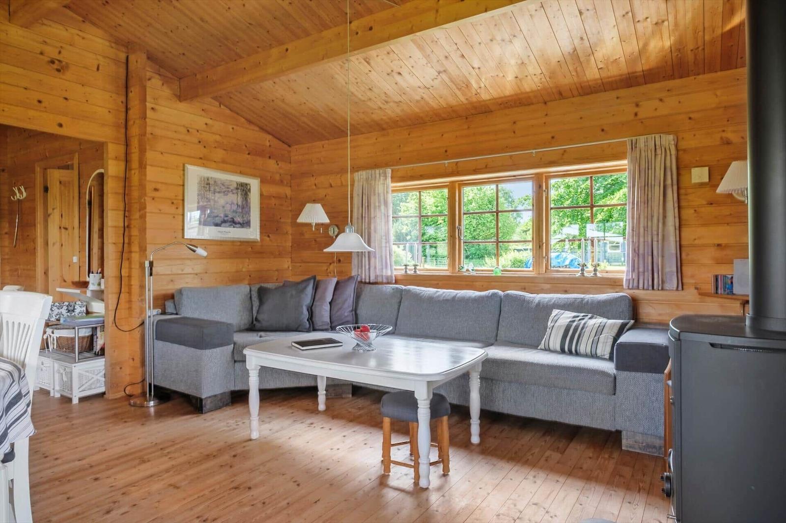 Wohnzimmer mit Holzwand, Sofa, Tisch und Fenster mit Blick auf Grün.