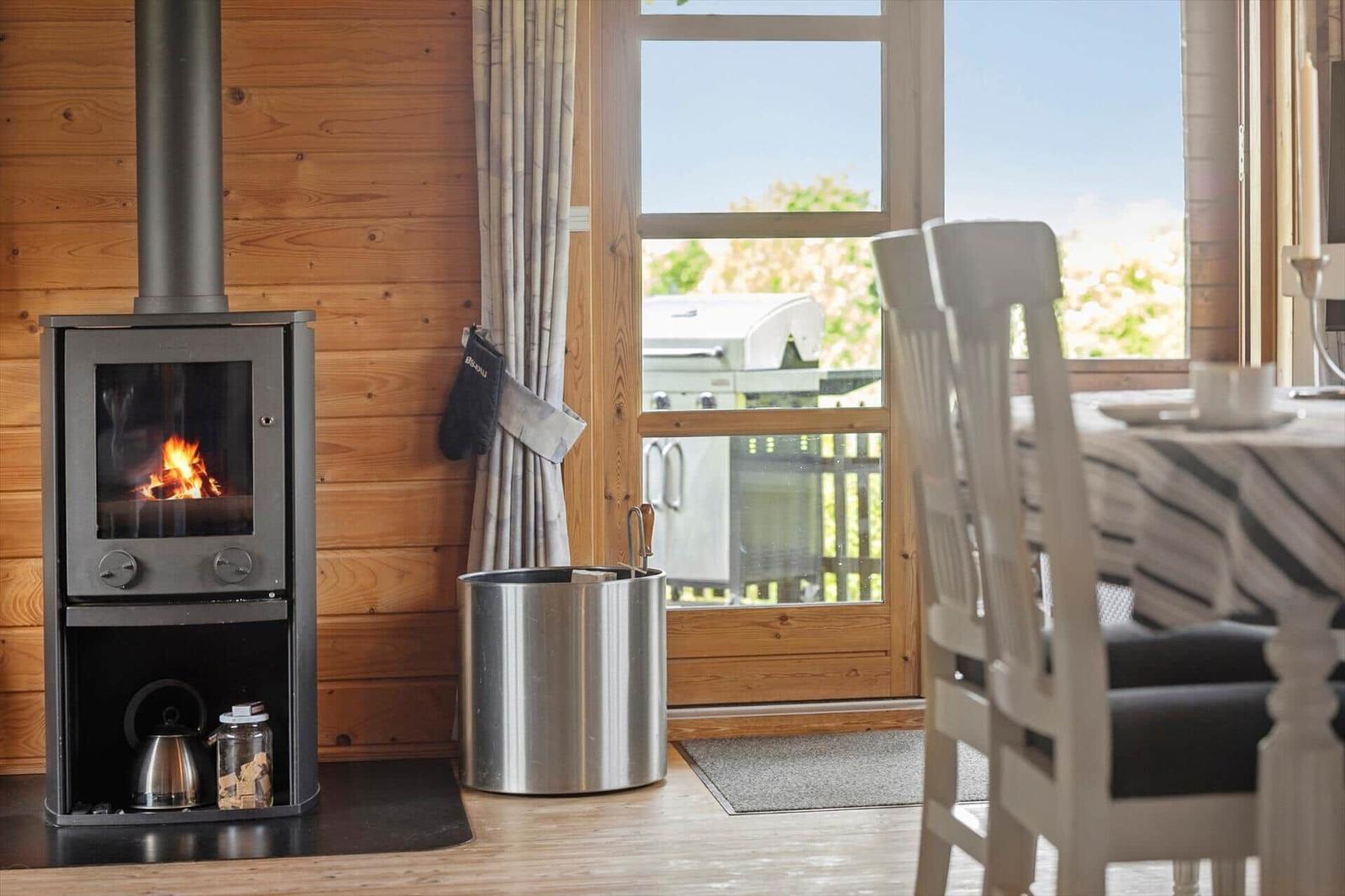 Kaminofen mit brennendem Holz, Essbereich mit Tisch und Stühlen, Fenster mit Blick auf Grill.