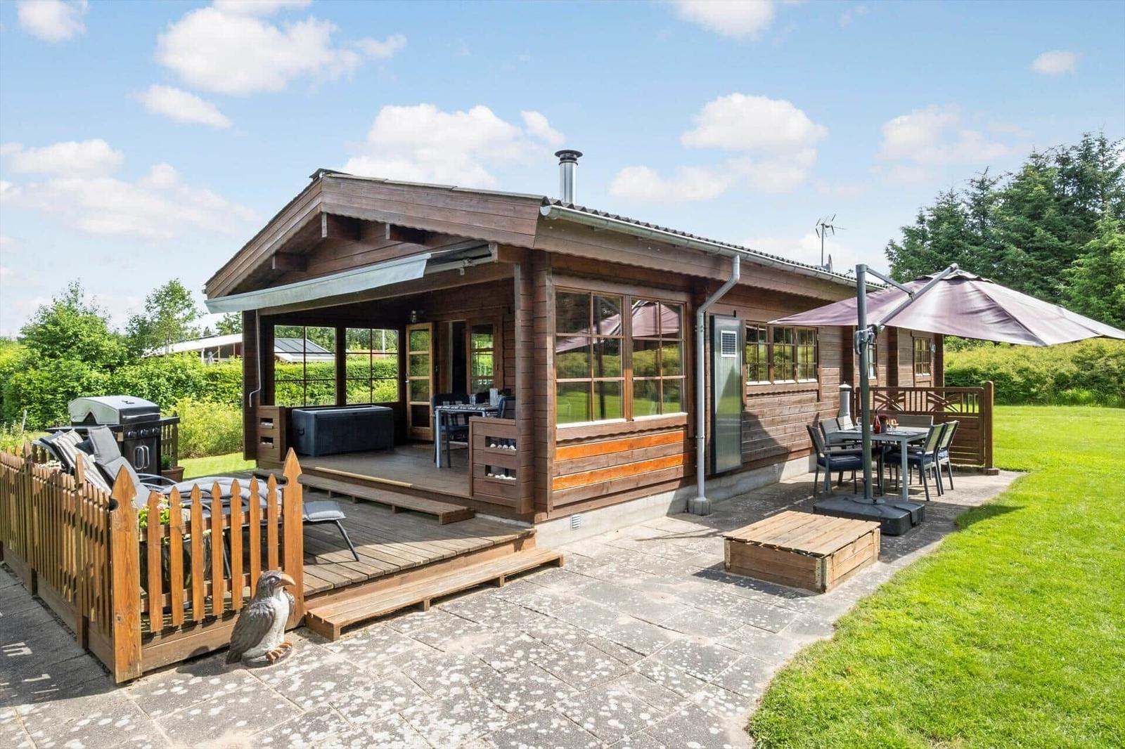 Holzhaus mit Terrasse, Grill und Sitzgelegenheiten im Garten.