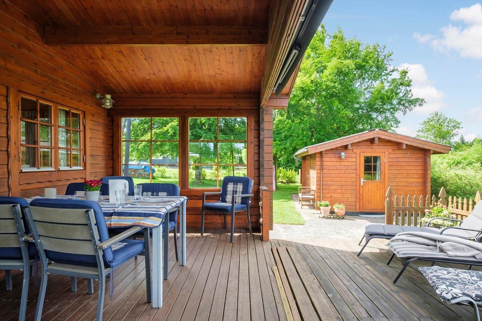 Terrasse mit Tisch und Stühlen, Holzhaus im Hintergrund, Garten mit Liegestühlen.