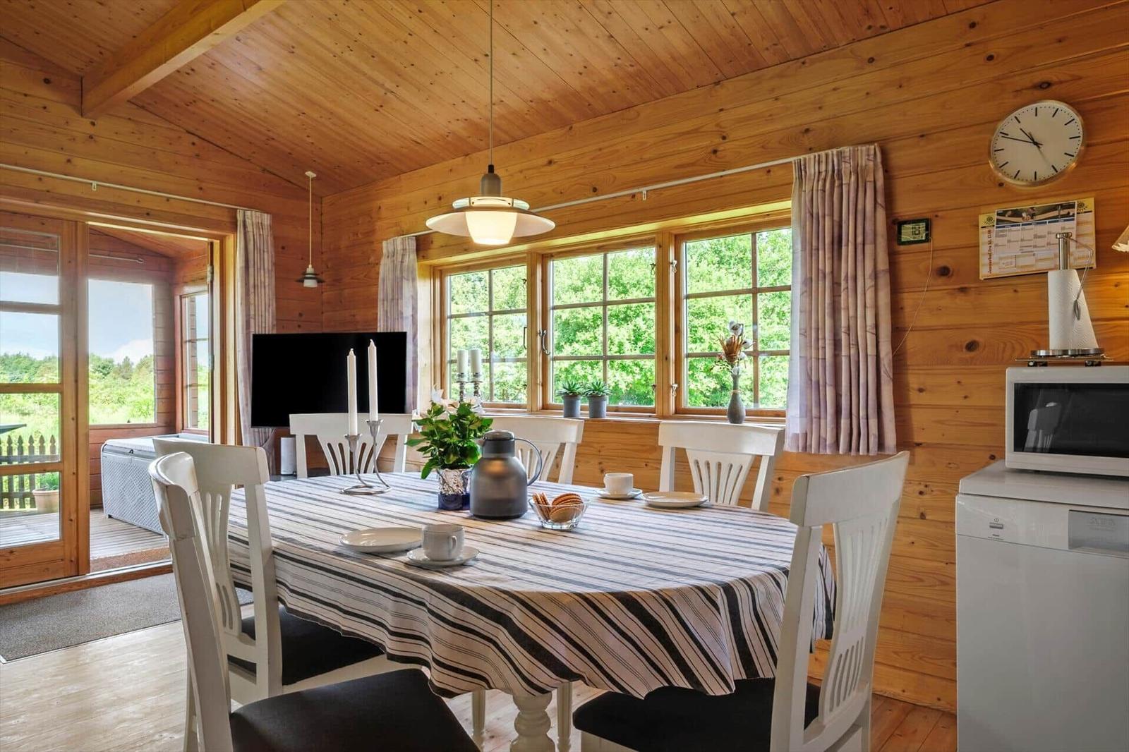 Esszimmer mit Holzwand, Tisch, Stühlen und Fensterblick auf Grün.