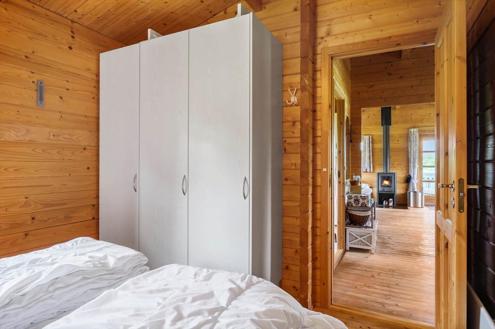 Schlafzimmer mit weißem Schrank und Blick in Wohnbereich mit Kaminofen.