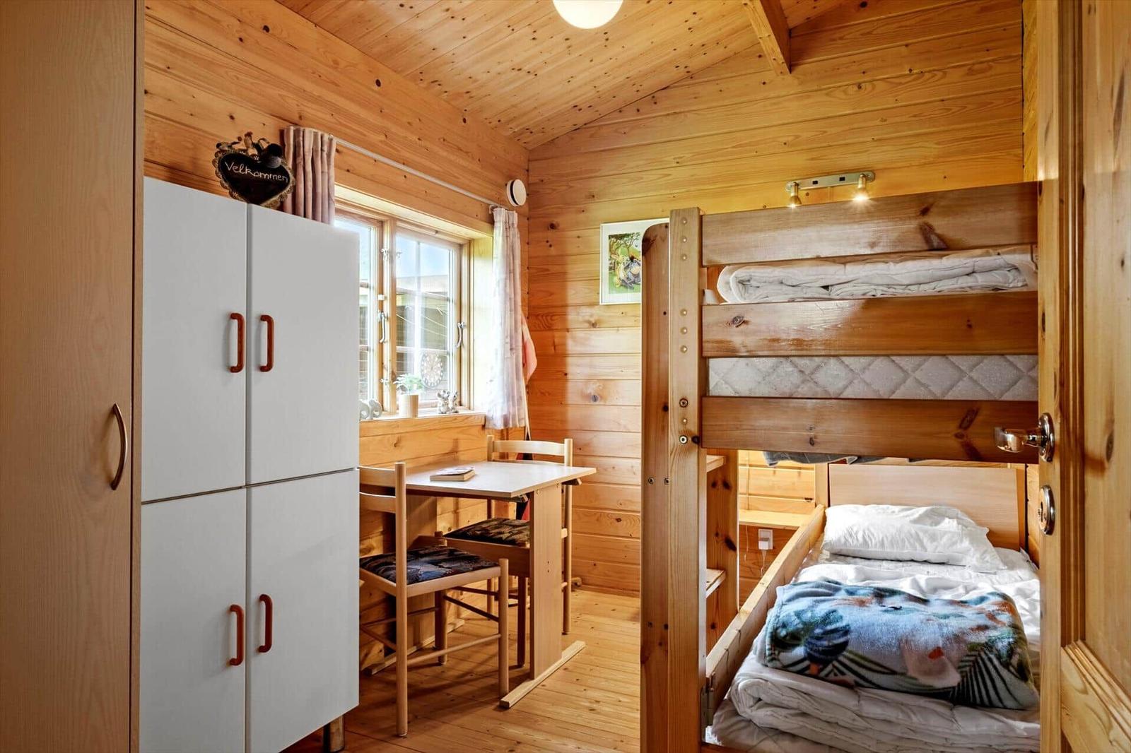 Schlafzimmer mit Doppelstockbett, Tisch und Schrank. Holzwände und -decke.