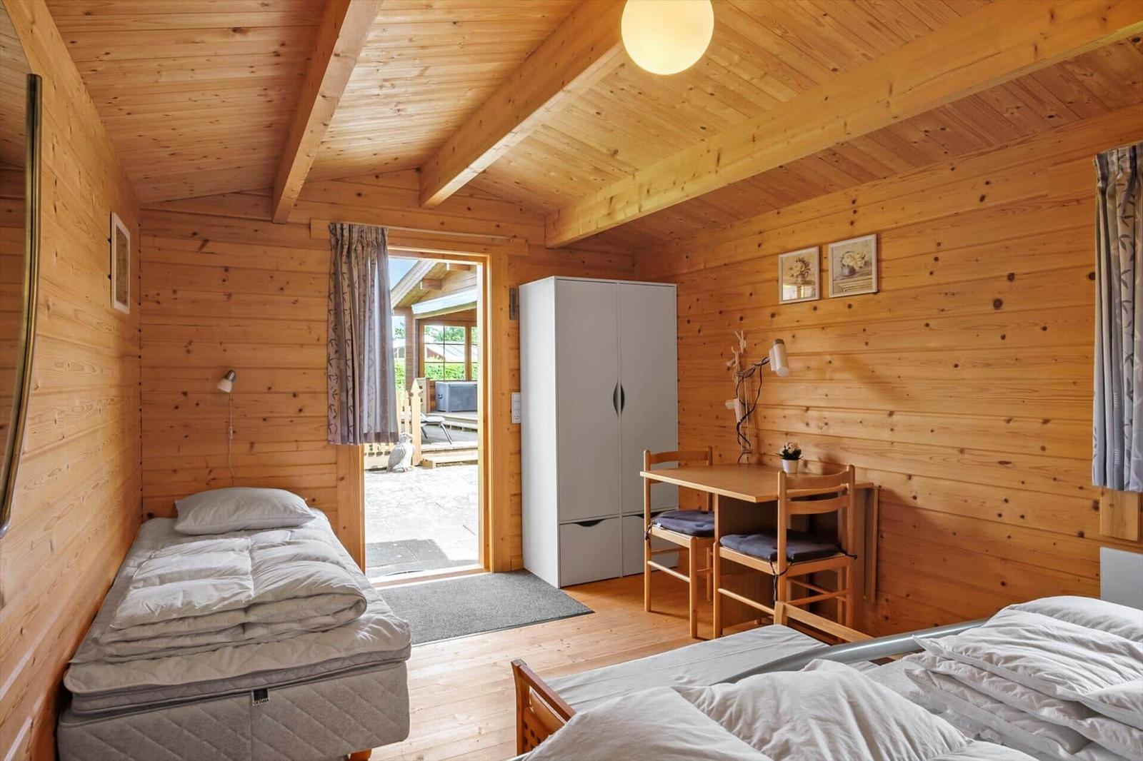 Zimmer mit zwei Betten, Schreibtisch und Kleiderschrank. Holzwände und Decke. Tür zum Außenbereich.