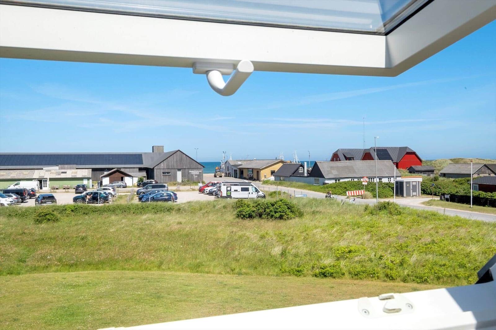 Blick vom Fenster auf einen Parkplatz mit Autos und Häusern am Meer.