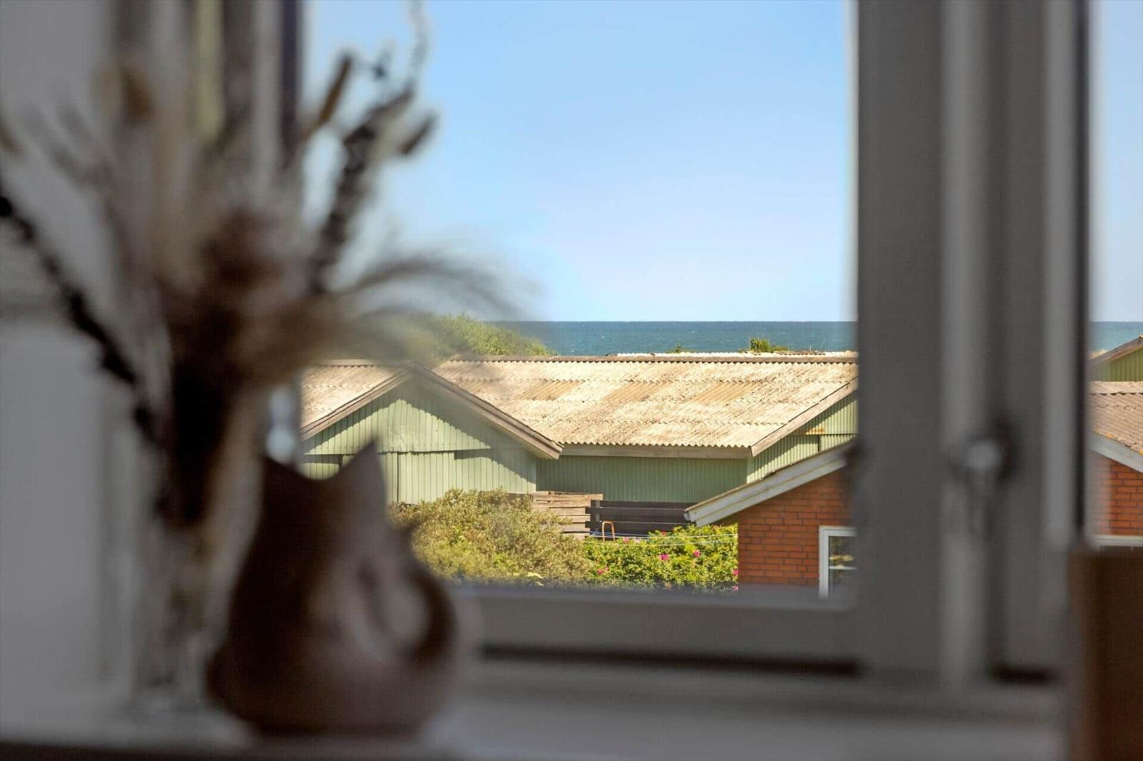 Durch das Fenster ist das Meer und ein Haus mit Wellblechdach zu sehen.