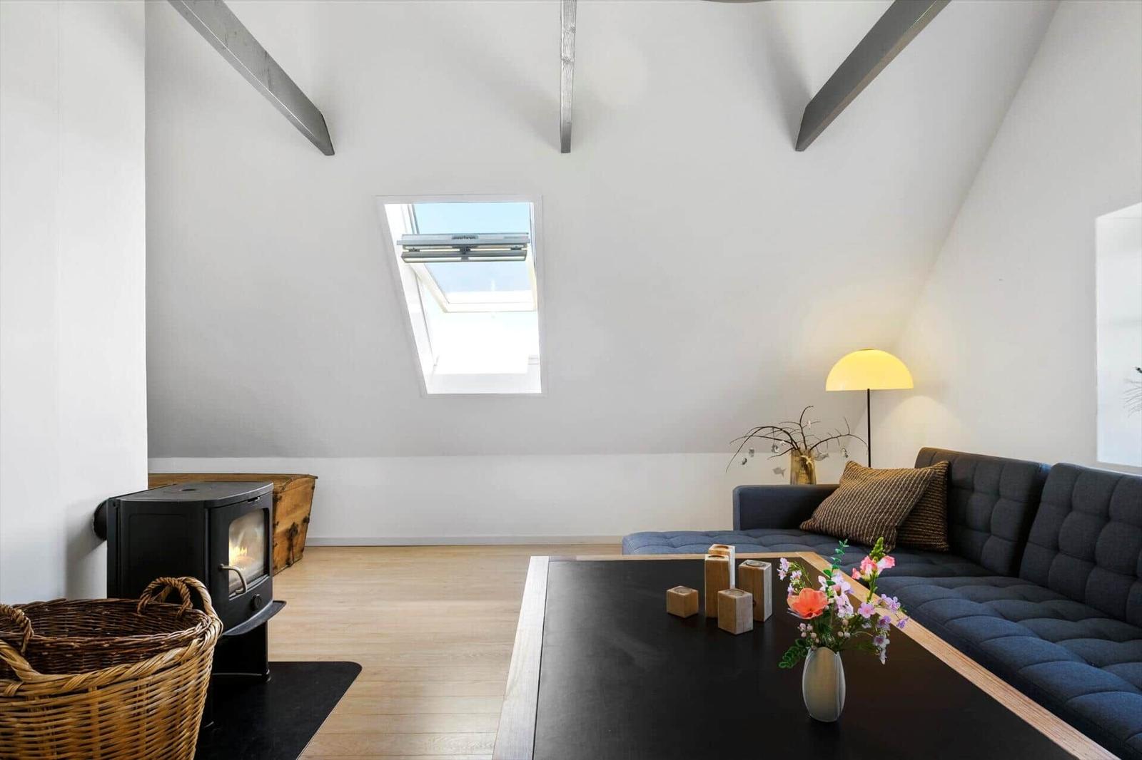 Dachgeschosswohnung mit Holzboden, Schiebedachfenster, Sofa und Kaminofen.