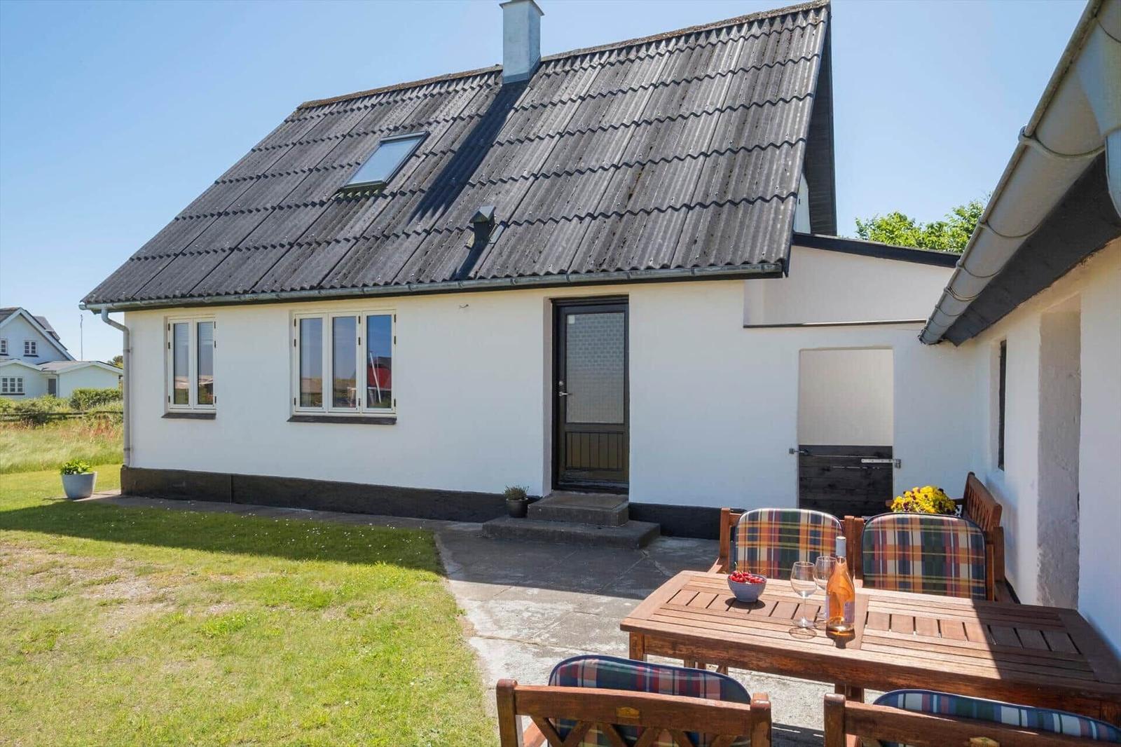 Wohnhaus mit Terrasse, Holztisch und Stühlen mit karierten Sitzkissen.